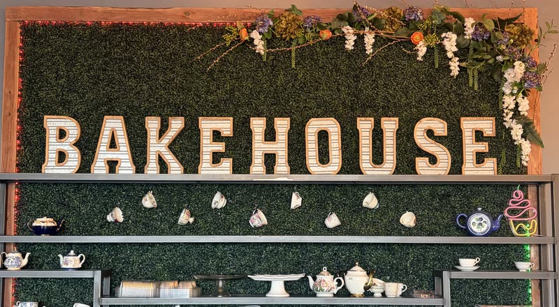Her teapots and teacups on the shelves under the BAKEHOUSE letters and a garland of flowers